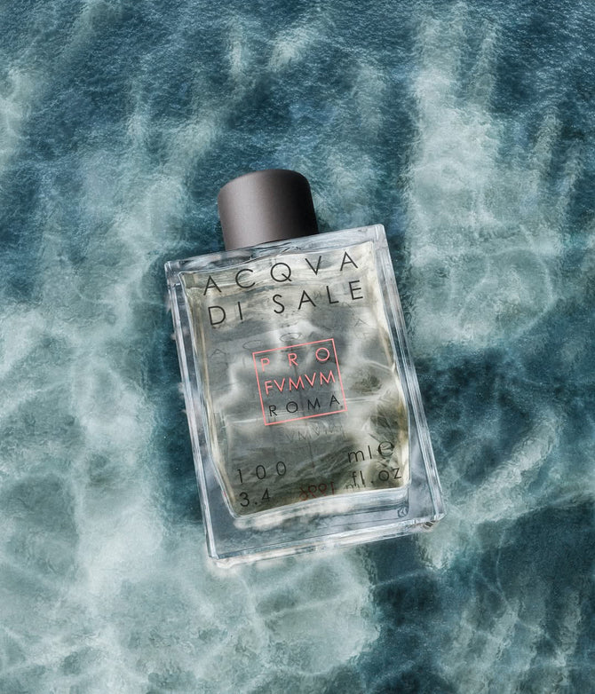Ein 100-ml-Parfumflakon des Duftes 'Acqva di Sale' der Marke Profumum Roma. Die rechteckige, transparente Glasflasche mit schwarzem Verschluss und dem charakteristischen Logo liegt auf einem Hintergrund, der an bewegtes, tiefblaues Meerwasser erinnert.